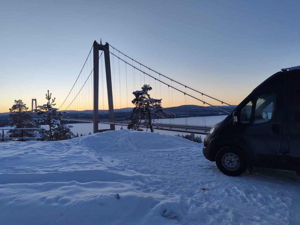 Wohnmobil auf Schnee, Brücke im Hintergrund über zugefrorenen See